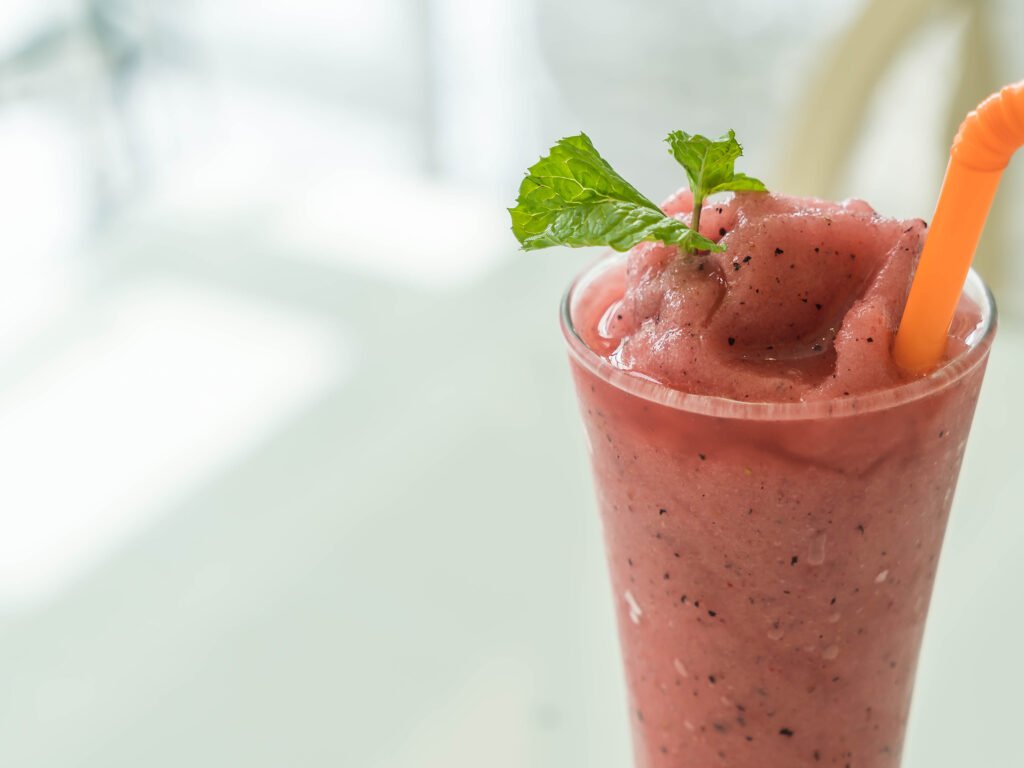 Taça de vidro com smoothie de acerola dentro. Uma folha de hortelã no copo para respirar e alcool/vodka.