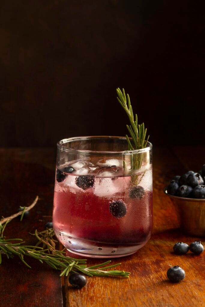 copo baixo com drink de amora, limão e gelo e alecrim