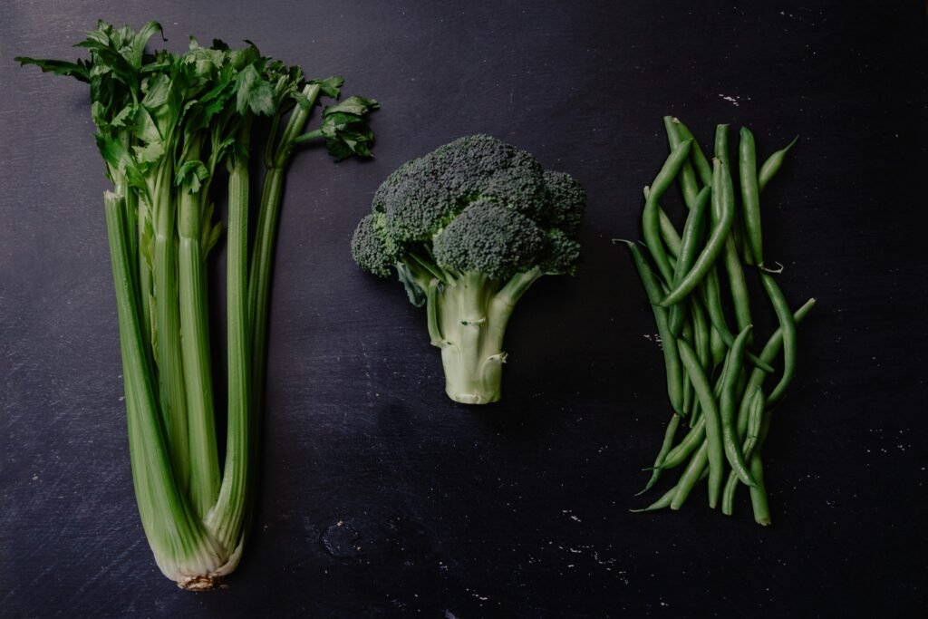Salsão, brócolis e vagens em um fundo escuro.