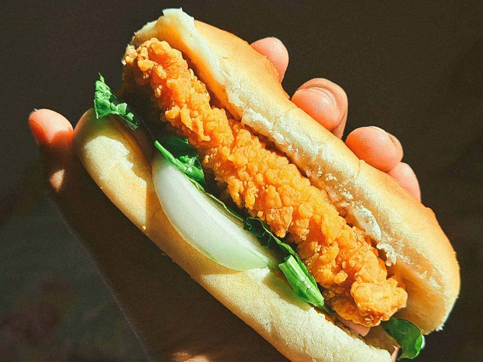 Hamburguer de grão de bico crocante já montado no pão com alface e cebola na mão de uma pessoa