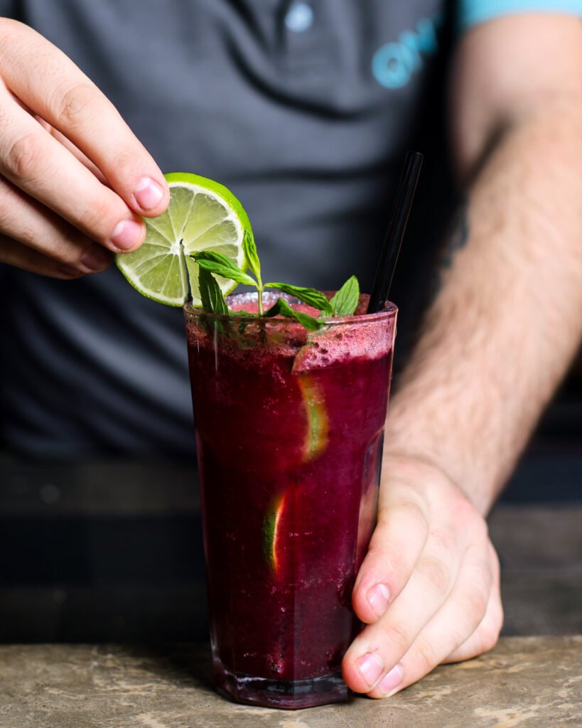 copo alto com mojito roxo, hortelã e amoras.