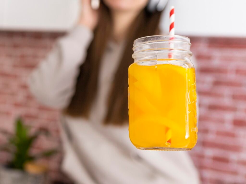 Caneca de suco detox de manga haden sendo segurada por uma mulher ao fundo desfocada